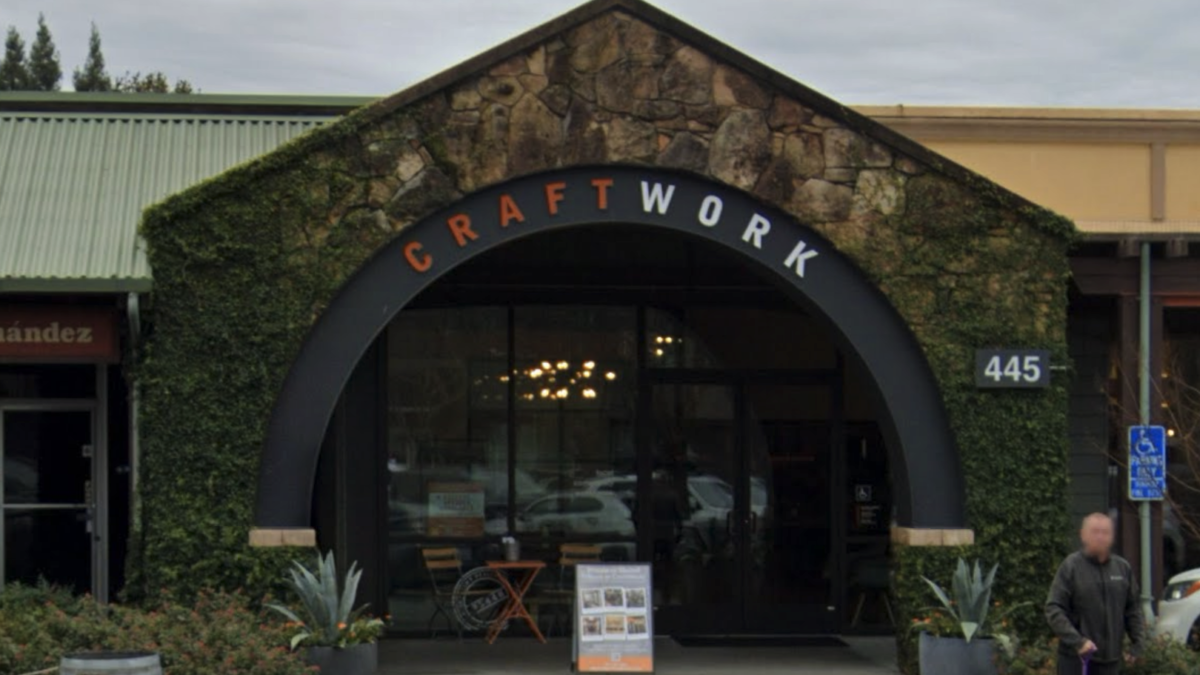 The front entrance of The Gold Drop , a modern coworking space at 445 Center Street, Healdsburg, CA, featuring a stone archway with greenery and glass doors leading inside.