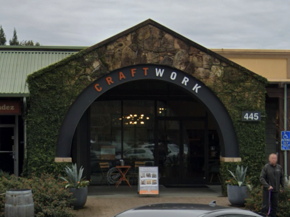 The front entrance of The Gold Drop , a modern coworking space at 445 Center Street, Healdsburg, CA, featuring a stone archway with greenery and glass doors leading inside.